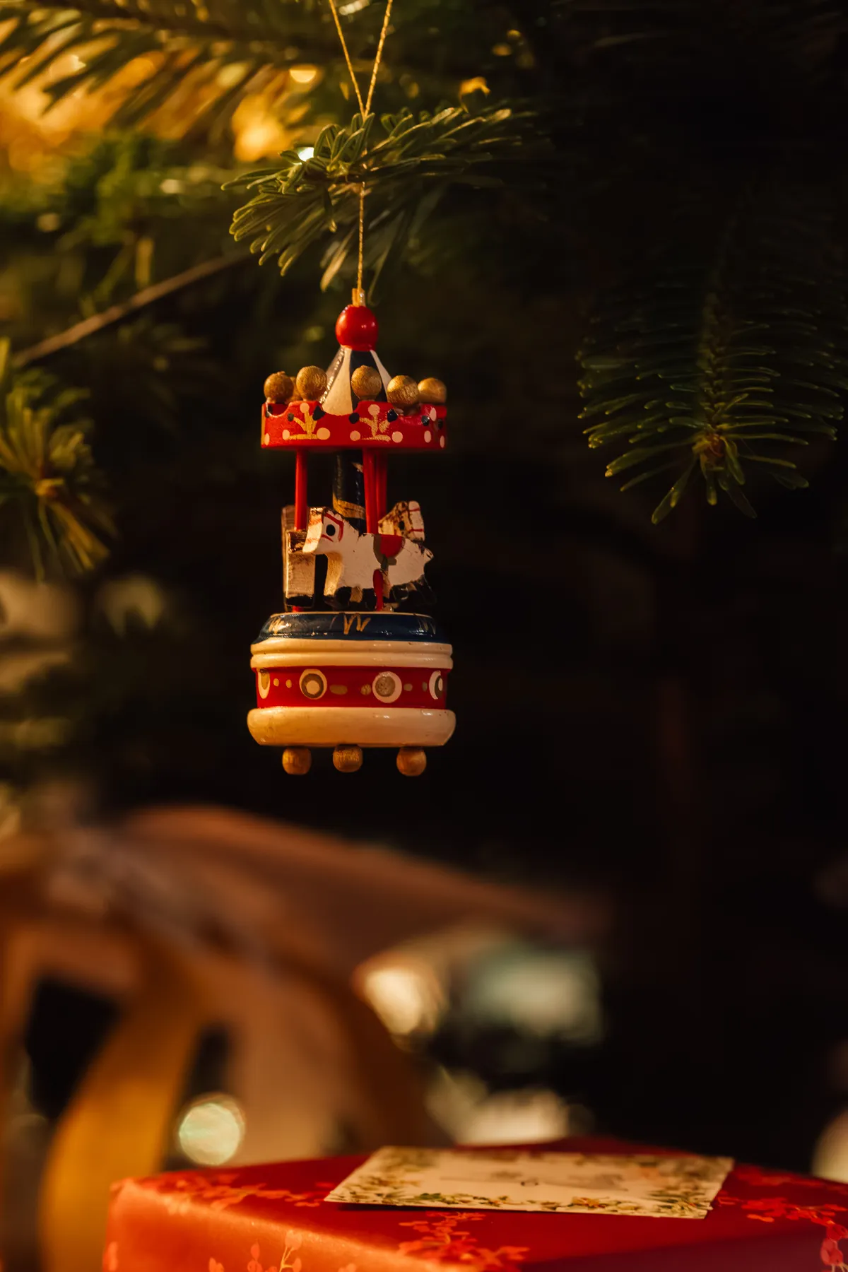 Festive Christmas carousel ornament hanging on a fir tree branch with warm holiday ambiance.