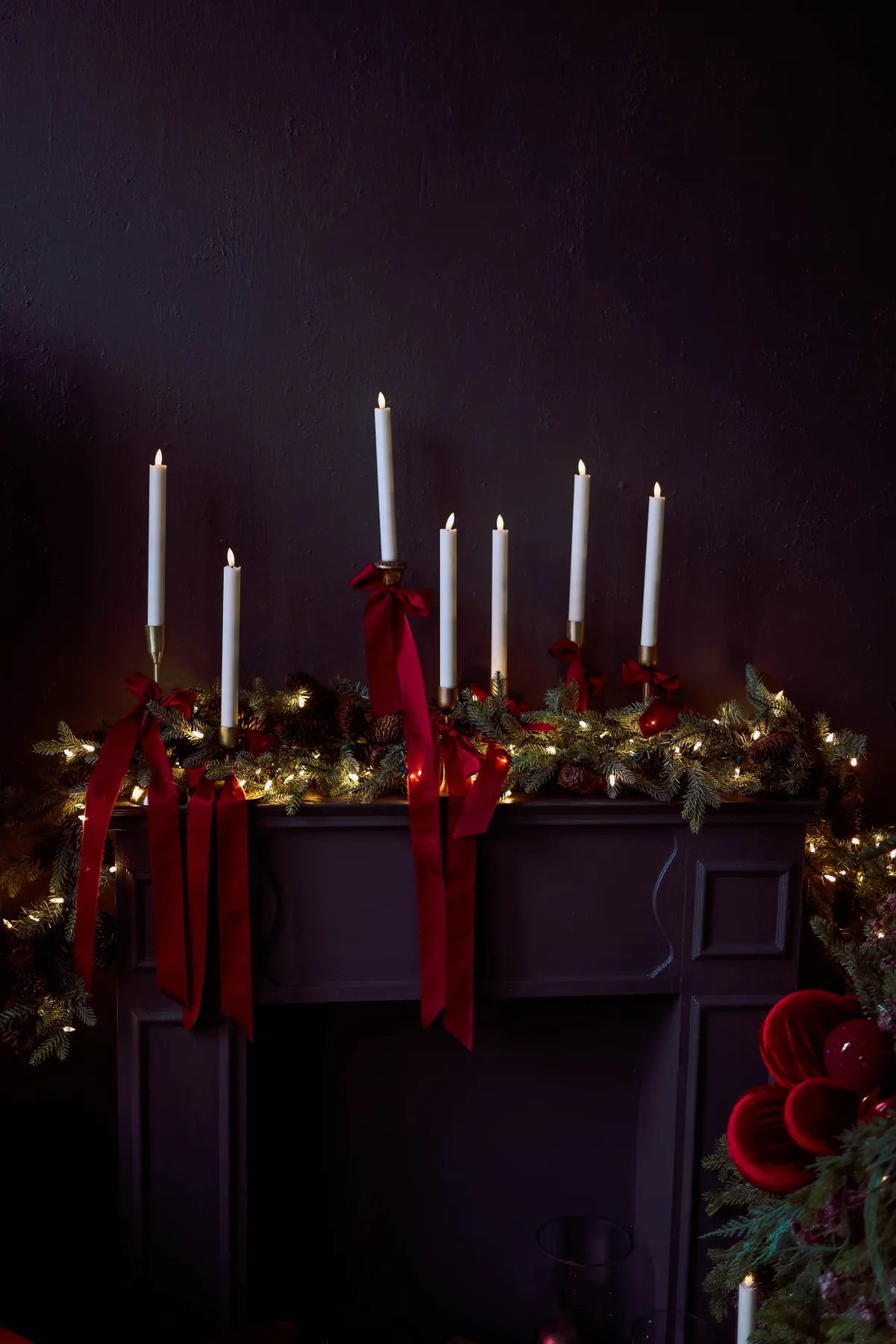Festive Christmas mantel decor with candles, garland, and red ribbons, creating a warm holiday ambiance.