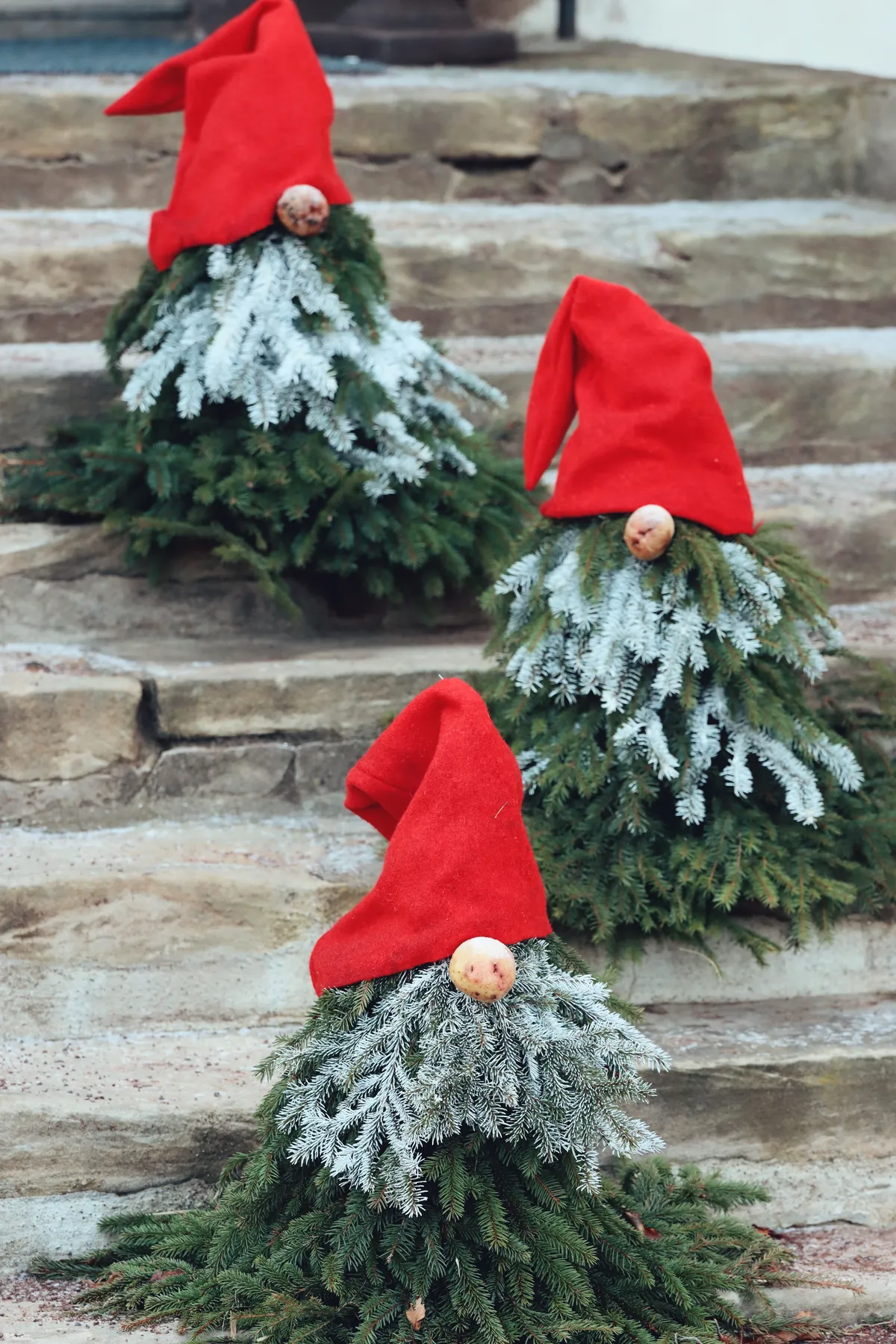 Festive gnome decorations with red hats and greenery displayed on stone steps.