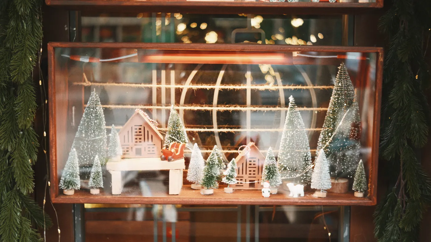 Festive miniature Christmas village with snow-covered trees in a warm window setting.