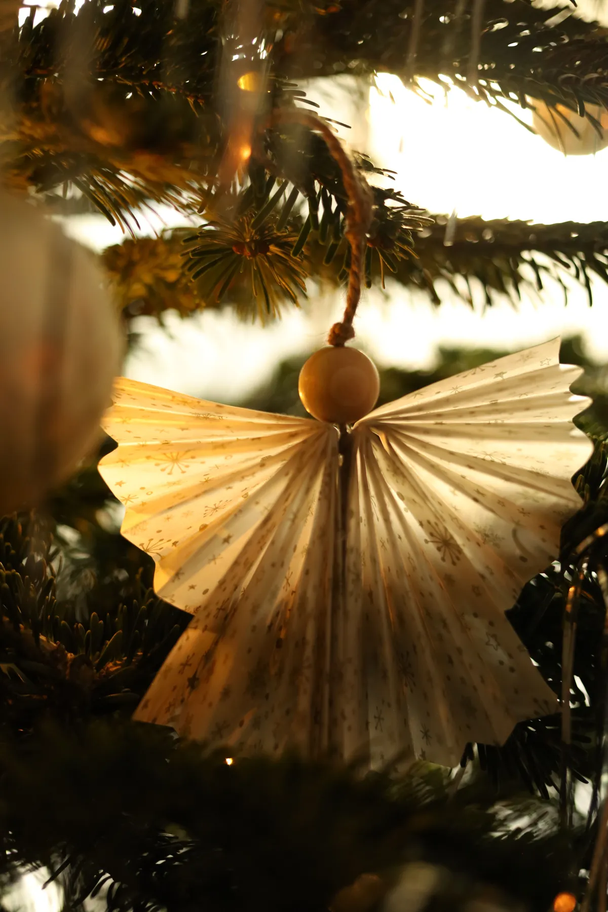 Festive paper angel ornament hanging on a Christmas tree branch