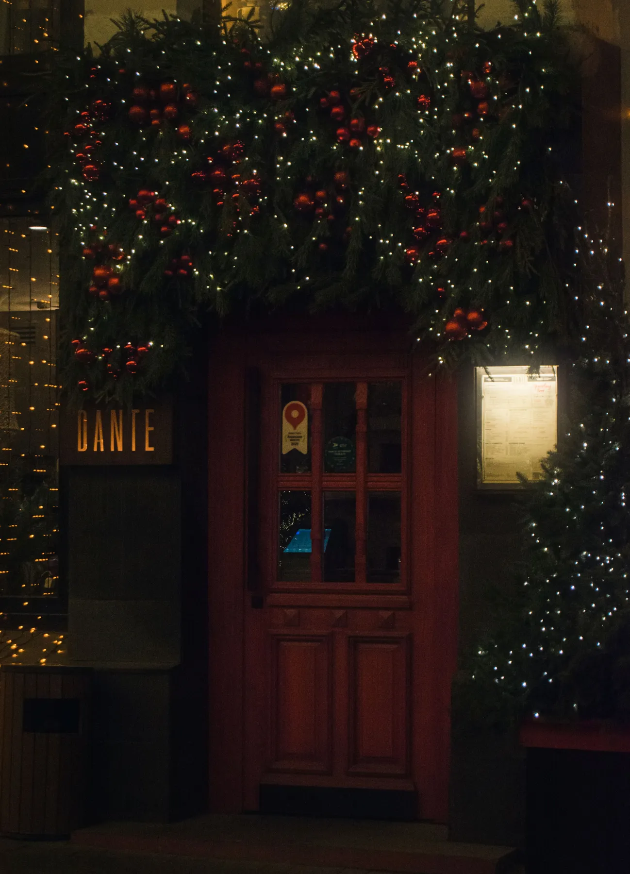 Festive restaurant entrance adorned with Christmas lights and pine garlands, creating a warm holiday atmosphere.