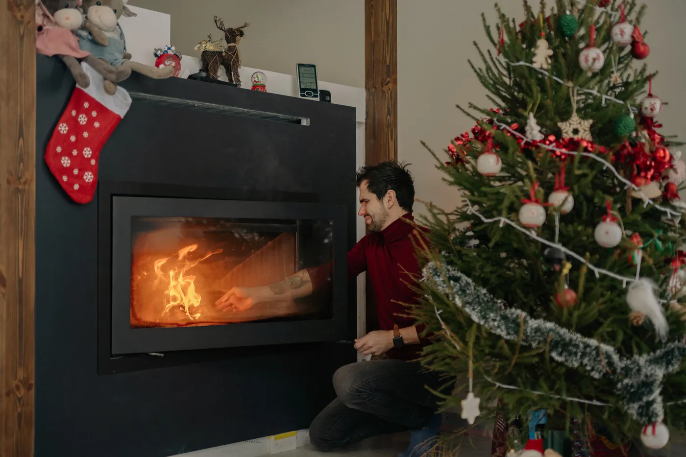 Man lighting a fire in a festive setting with a decorated Christmas tree.