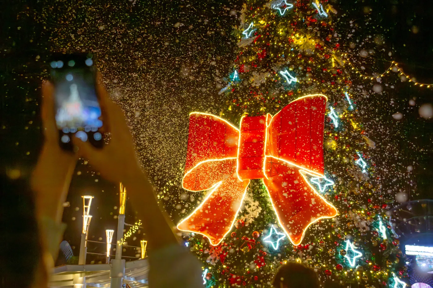 Person films illuminated christmas tree with large red bow