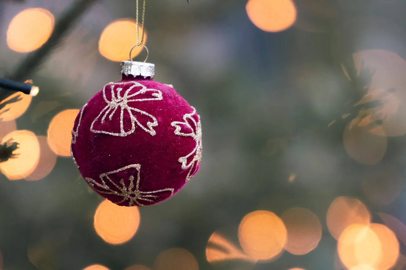 Red Christmas ornament with gold designs on a tree, featuring festive bokeh lights.