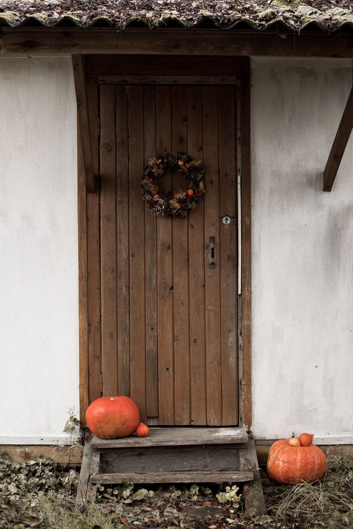 Rustic wooden door decorated with autumn wreath and pumpkins for Halloween celebration.