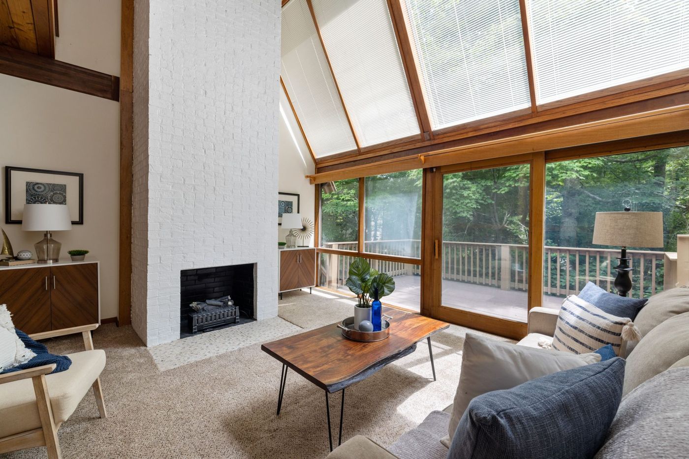 Spacious living room features a white brick fireplace and floor-to-ceiling windows overlooking greenery.