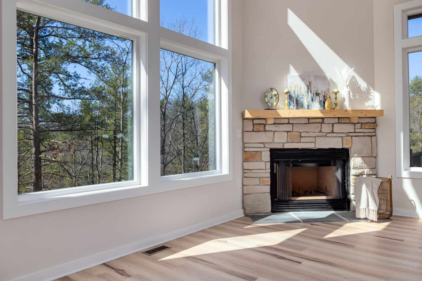 Spacious modern living room featuring large windows and a stone fireplace mantel.
