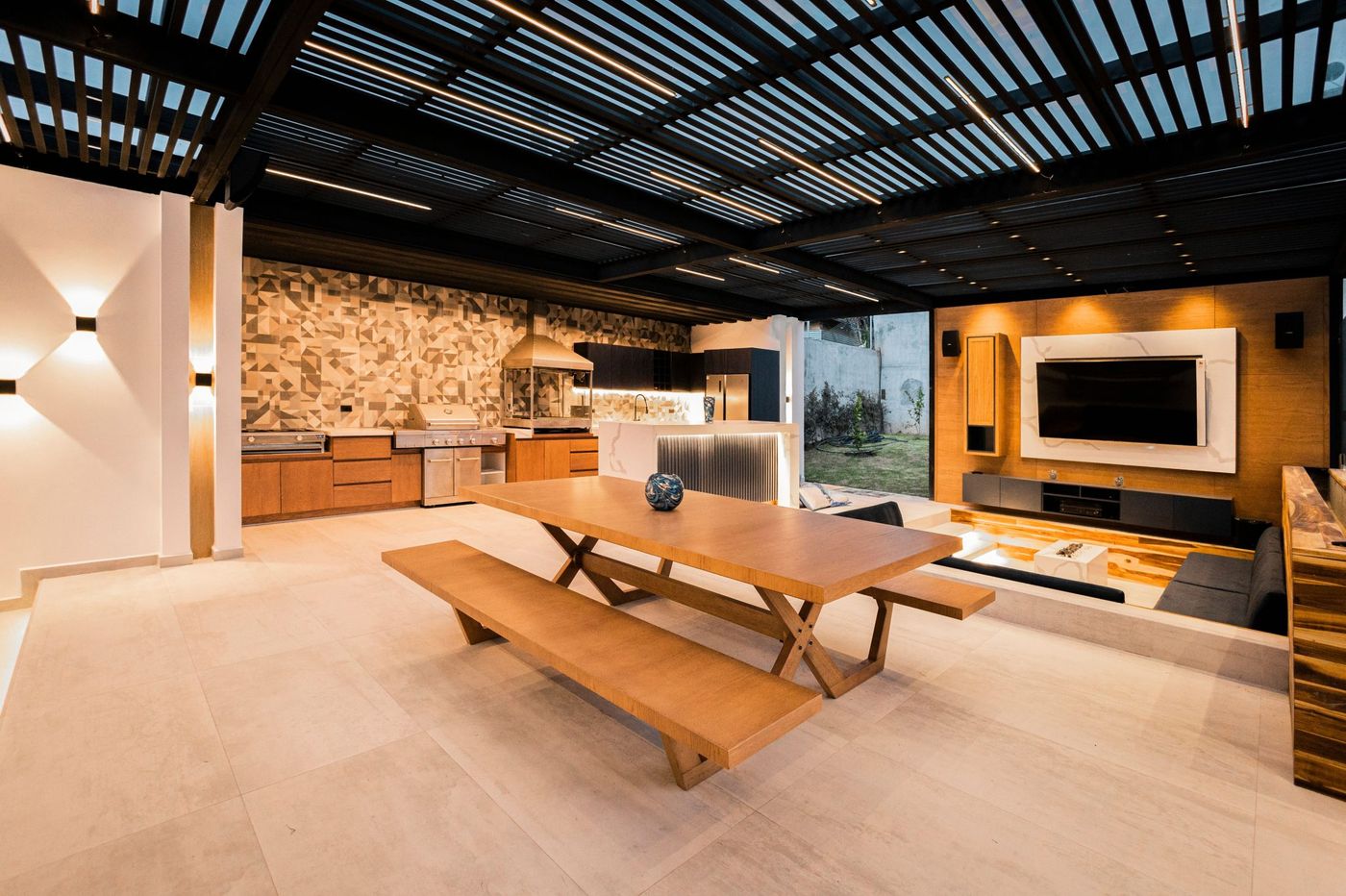 Spacious outdoor kitchen and living space featuring sleek design, wood accents, and a mounted TV.