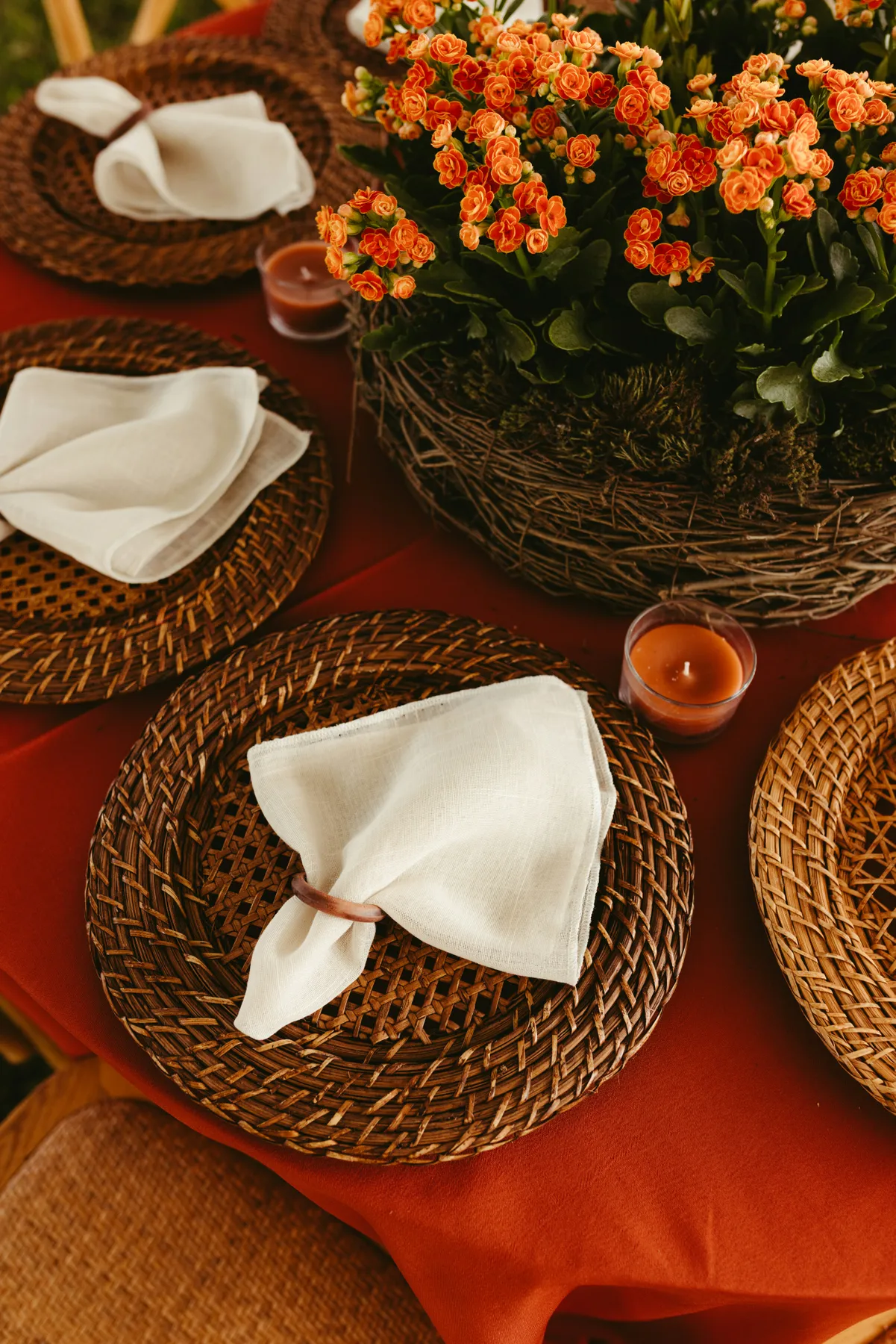 Table setting with woven placemats, white napkins, and orange flowers