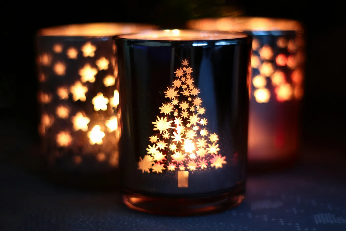 Three illuminated christmas candle holders with festive designs
