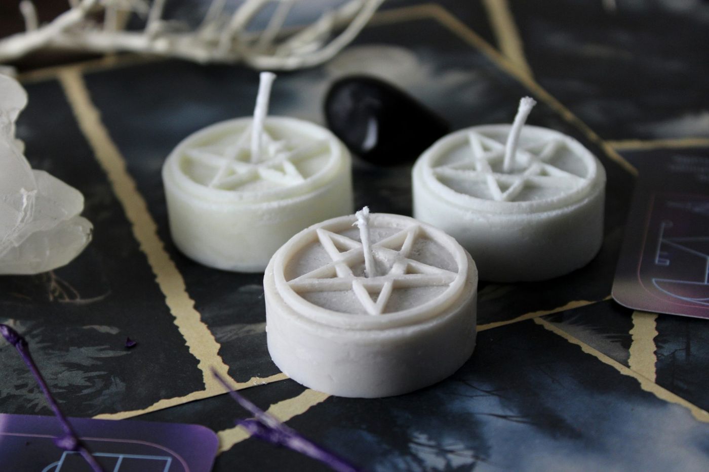 Three white wax candles with pentagram symbols on a dark surface