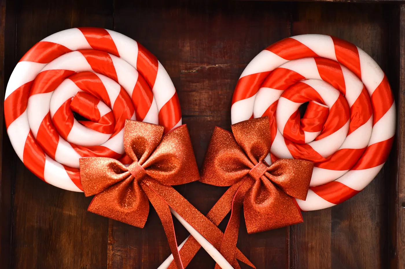 Two red and white striped lollipops with glittery bows, perfect for holiday celebrations.