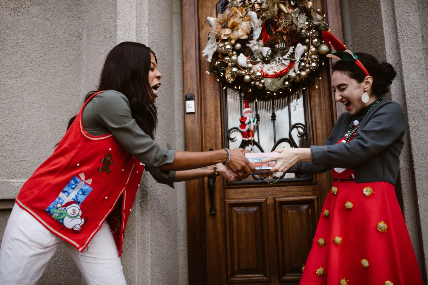 Two women enjoying a playful gift exchange at a beautifully decorated front door, celebrating Christmas.