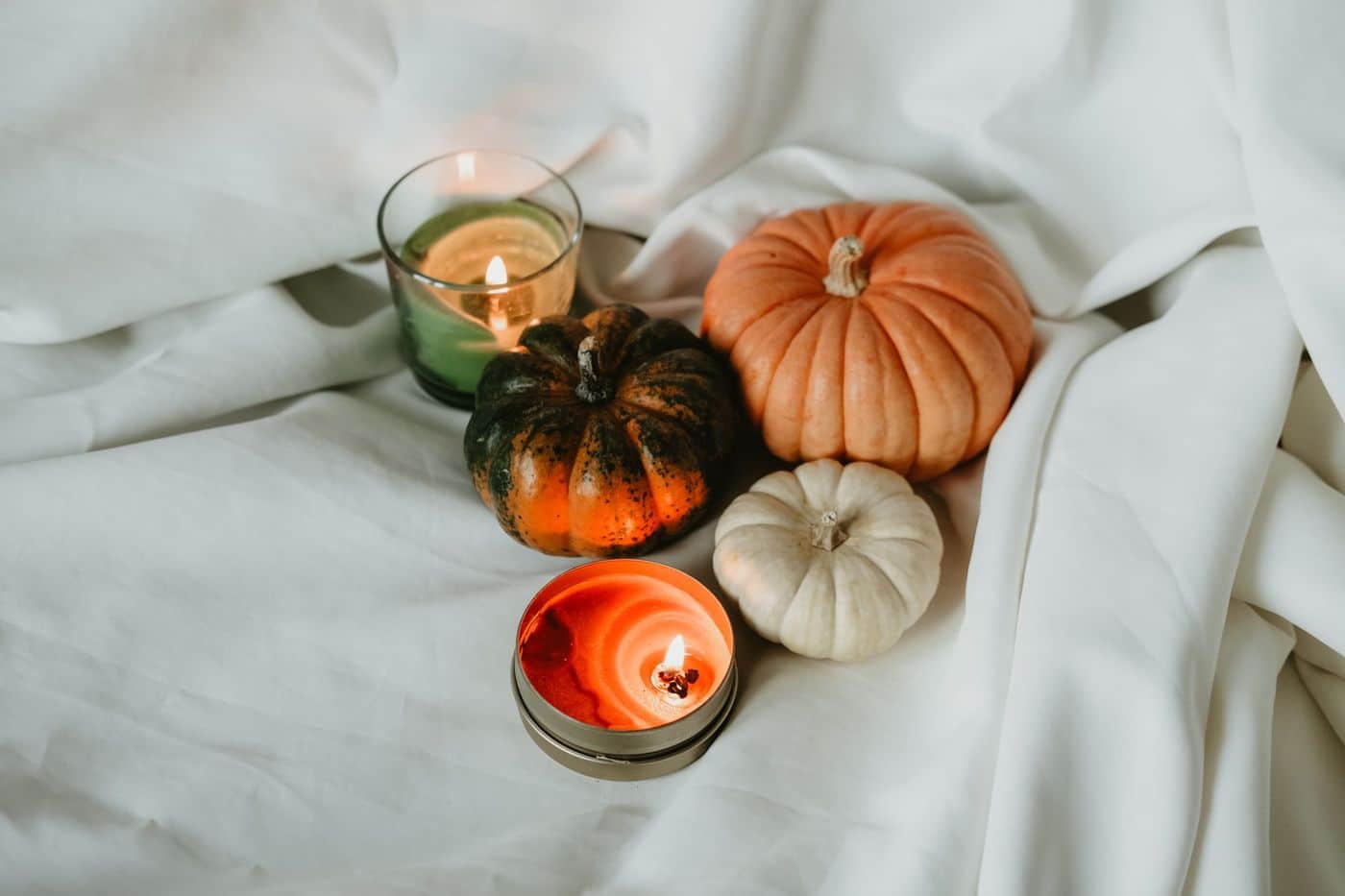 Warm ambiance with pumpkins and candles on a white sheet, perfect for fall-themed occasions.
