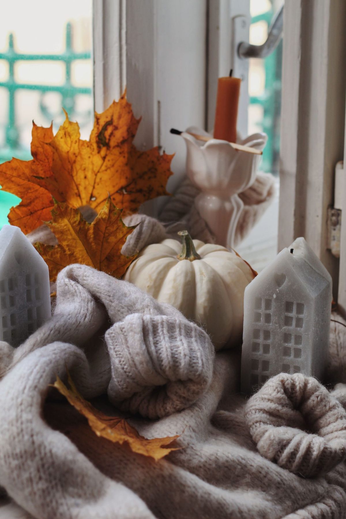 Warm and cozy autumn setting featuring a white pumpkin, candles, and fall leaves by a window.