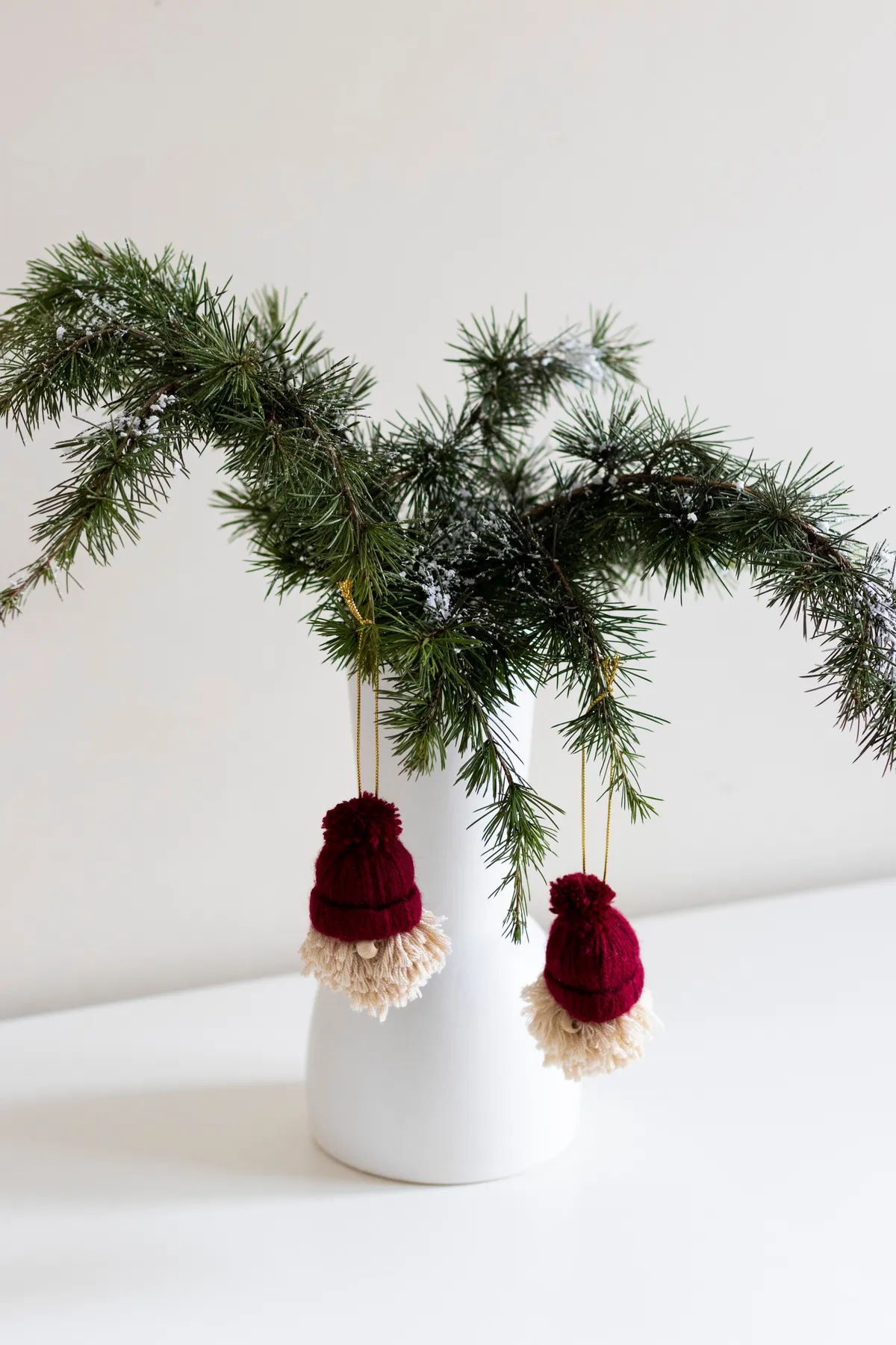 White vase with pine branches and red Christmas ornaments on a white background.