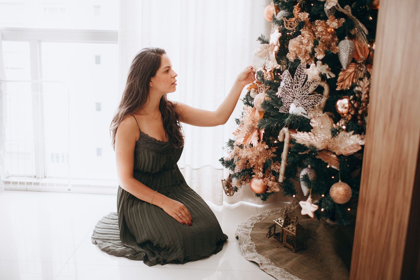 Woman decorating a festive Christmas tree indoors, adding ornaments.