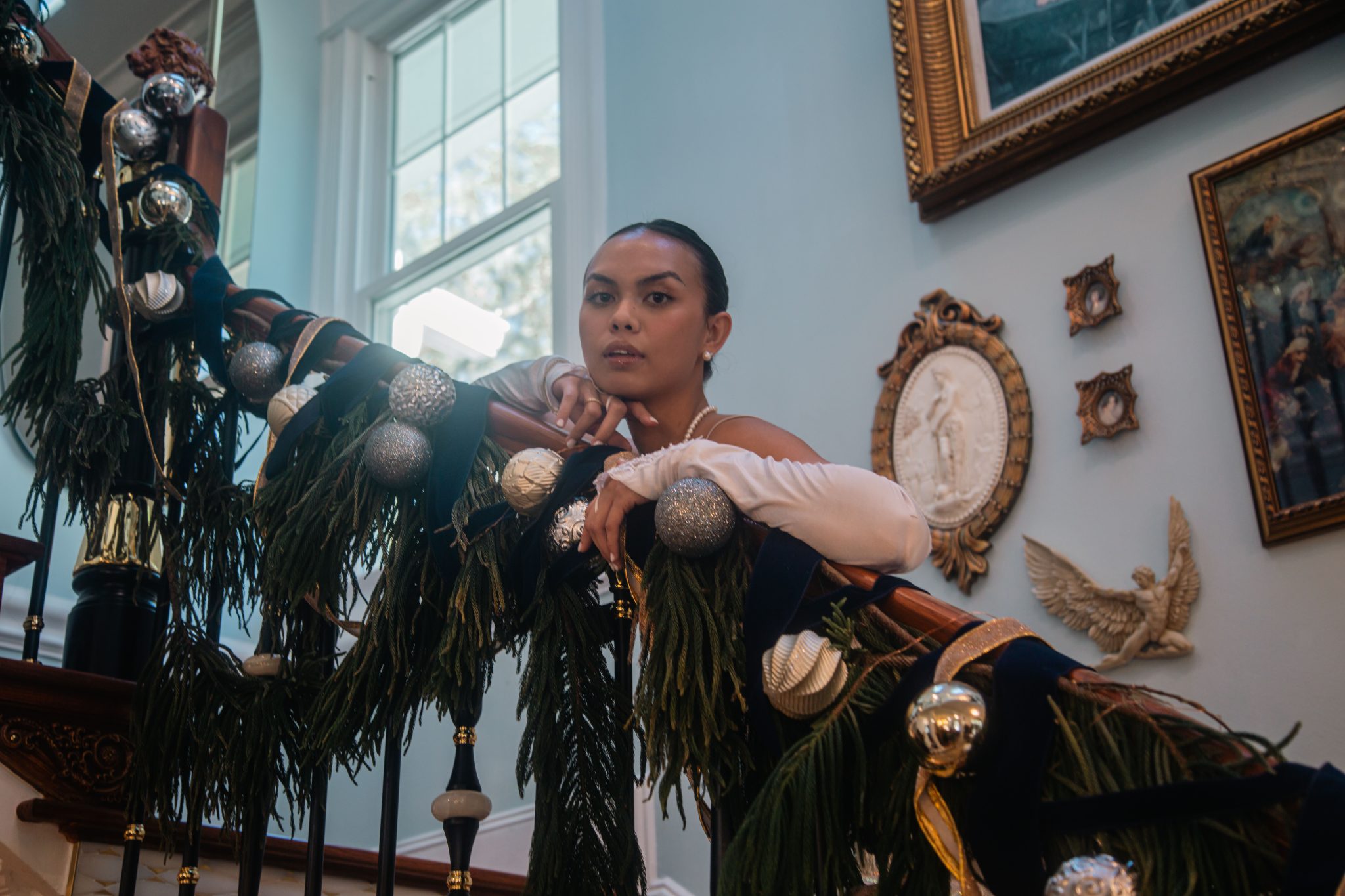 Woman posing on a beautifully decorated holiday staircase indoors.